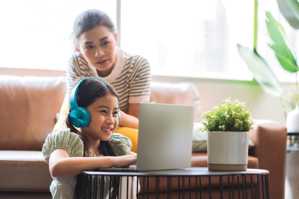 a mom and daughter using a laptop and headphones