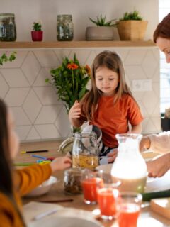 A mom and her children gathered in the kitchen, preparing and enjoying breakfast together around a counter filled with food and drinks.