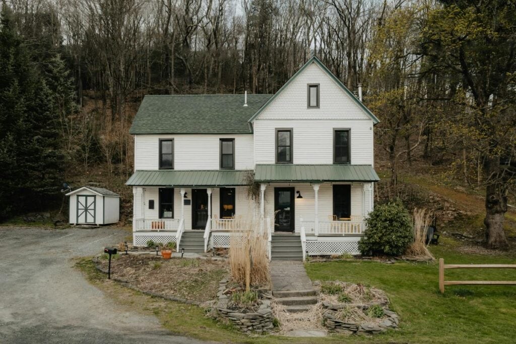 A traditional farmhouse with a green metal roof and dual front entrances, blending historic character with signs of modern upkeep.