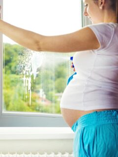 pregnant woman spraying window cleaner on an open window