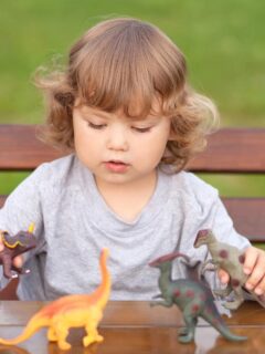 a toddler sitting outdoors playing with dinosaur toys on a table