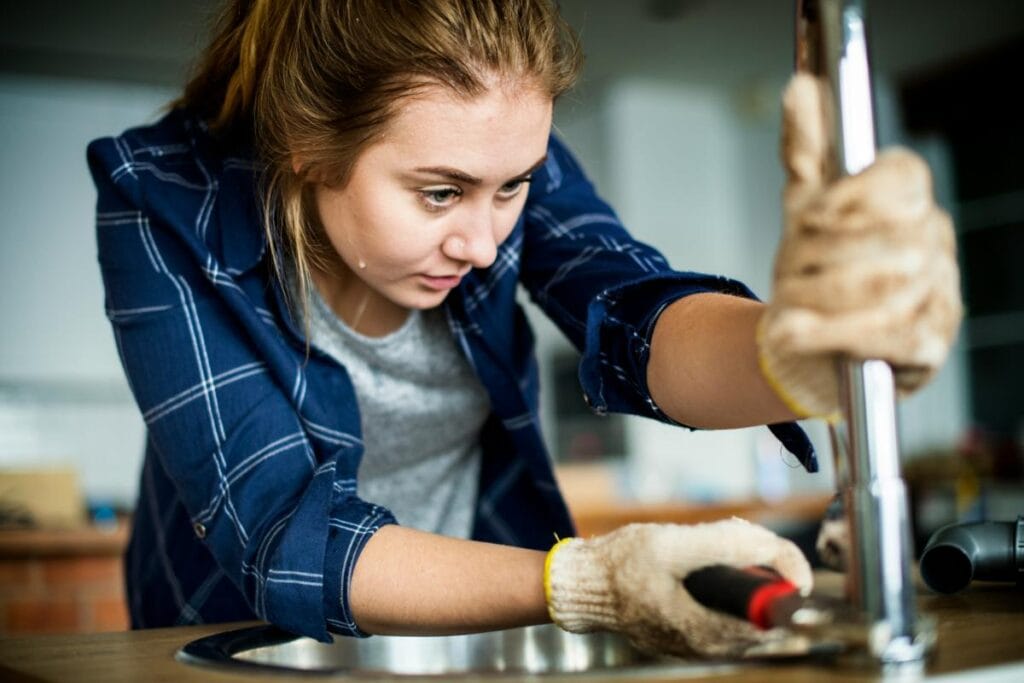 Focused woman repairing a kitchen sink, representing early plumbing fixes that help prevent leaks, water damage, and larger system failures.