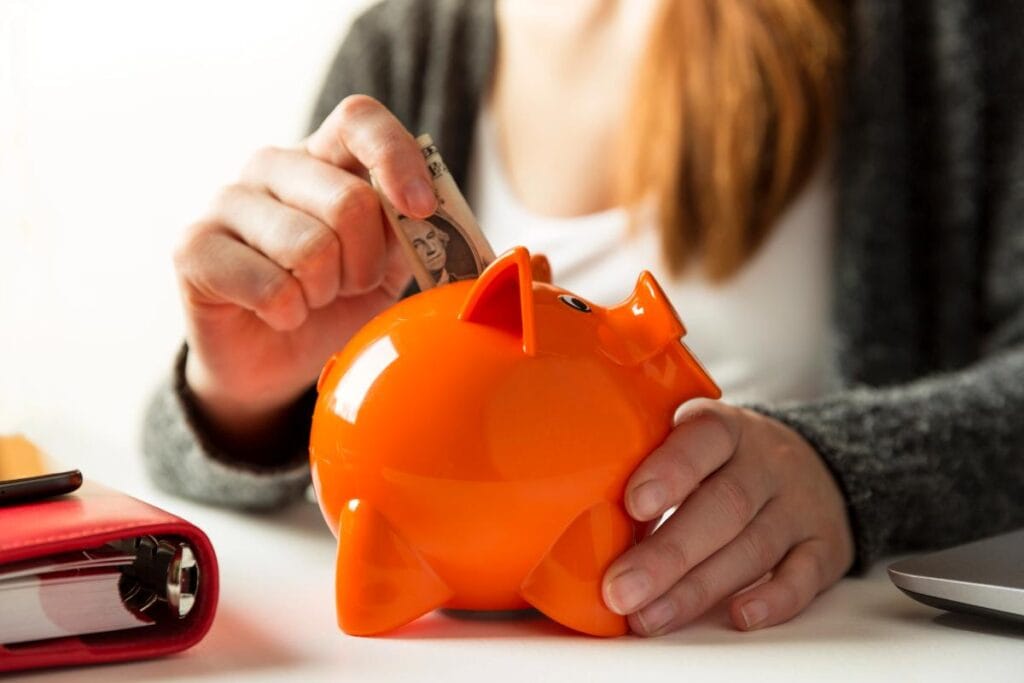a woman putting cash into an orange piggy bank to focus on financial self-care