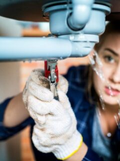 a female plumber working on a leaky pipe under the sink