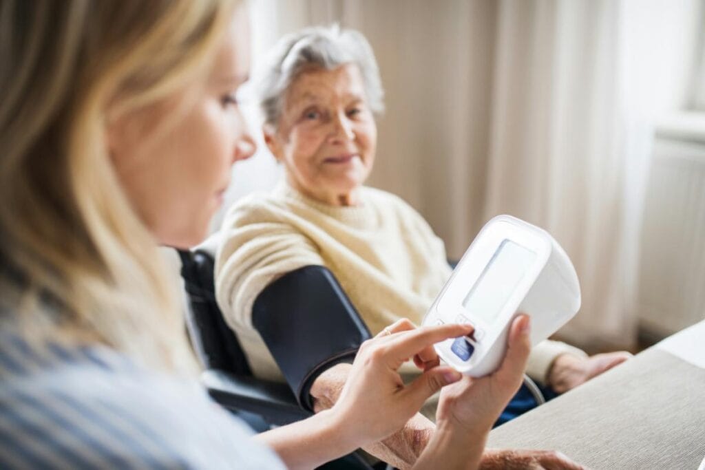 A caregiver checks the blood pressure of an elderly woman at home, highlighting attentive health monitoring in a supportive environment.