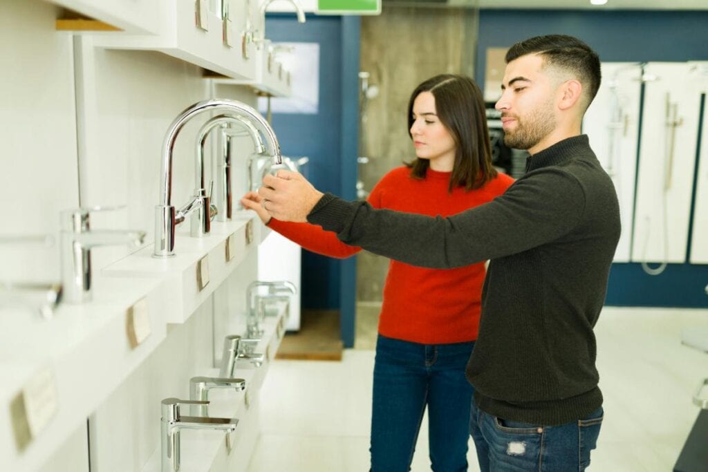 A man and woman comparing chrome faucet fixtures on display in a store while planning a bathroom remodel.