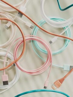 A colorful assortment of USB, Ethernet, and charging cables in pastel shades of pink, teal, white, and orange, coiled and spread out on a light surface.