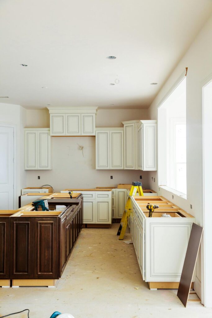 A kitchen mid-renovation with new cabinets being installed, power tools on counters, and a ladder in place, showing a major layout and design upgrade.