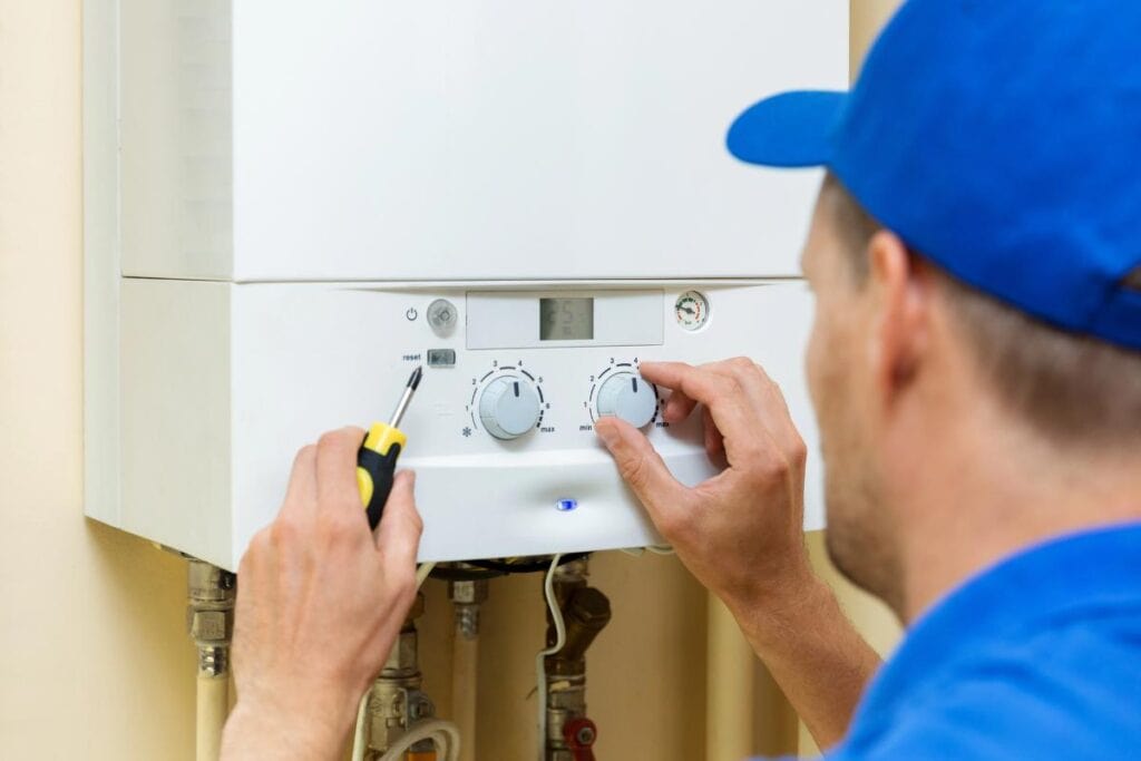A heating professional adjusting the controls on a home boiler system with a screwdriver during routine maintenance.