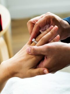 man sliding ring onto woman's finger proposing