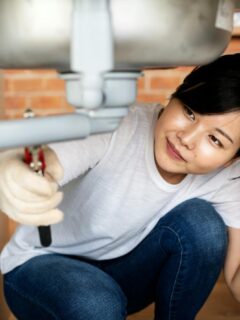 woman using a wrench on pipes under the sink