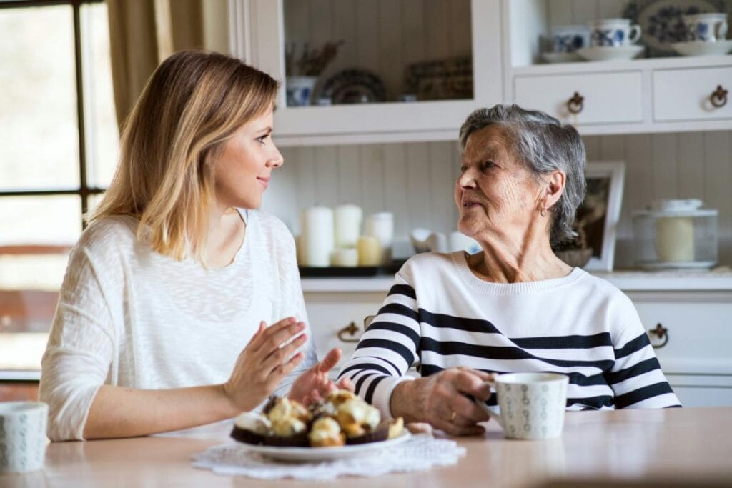 A young woman has a thoughtful conversation with her elderly grandmother over coffee and pastries, reflecting meaningful family connection.