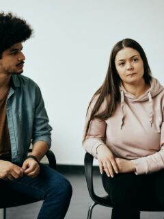 A young couple participates in a counseling session, seated and listening intently to a therapist during a relationship support group or therapy meeting.