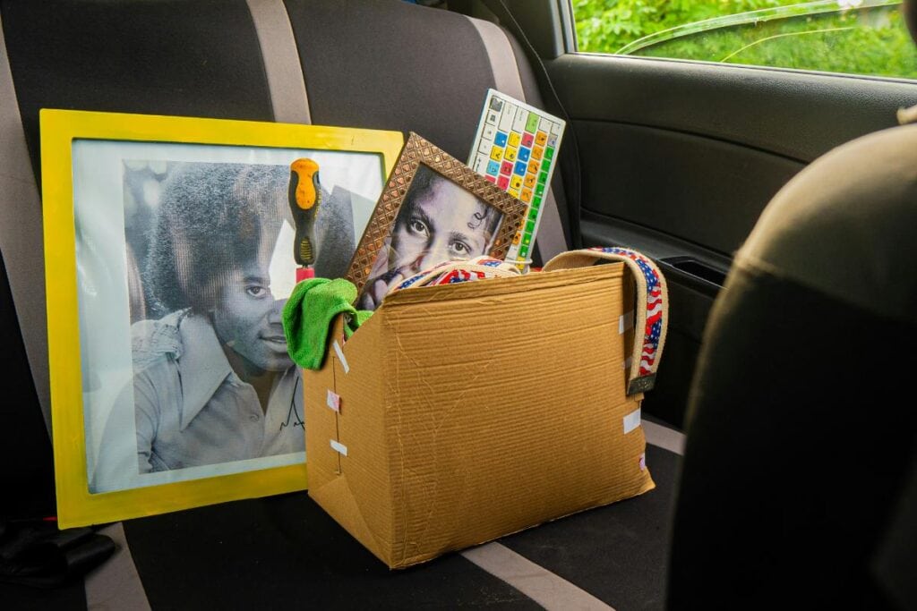 A cardboard box filled with personal items, framed photos, and tools sits on the back seat of a car, ready for a move.