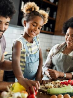 young daughter and her parents making food together in the kitchen