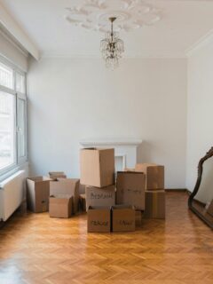 A nearly empty room with stacked labeled moving boxes and a decorative mirror leaning against the wall, ready for relocation