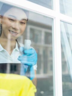 a smiling woman spraying window cleaner on the window glass - view is from the outside looking in