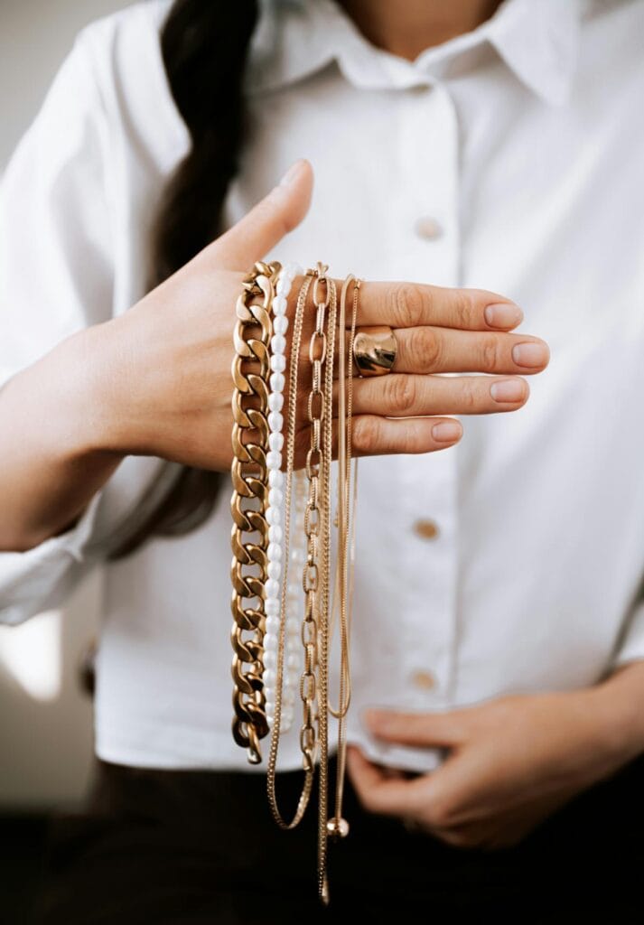 Woman holding a selection of simple gold necklaces and bracelets that easily elevate an everyday outfit.