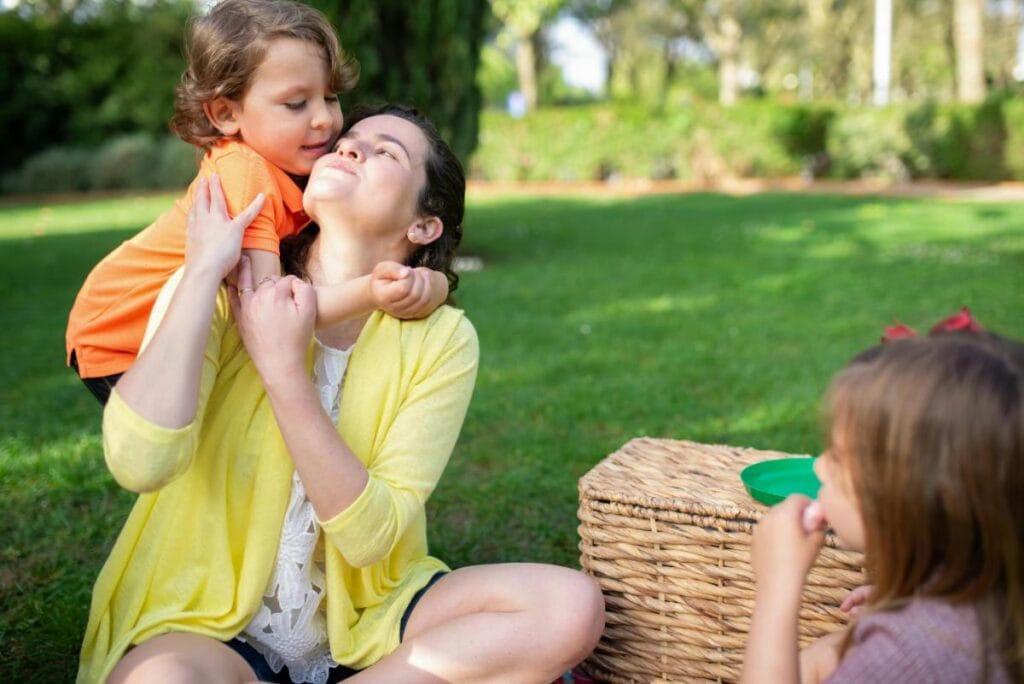 little boy in orange shirt hugging mother while sister looks on