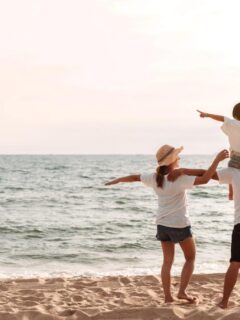 family of 3 walking along the beach, child on dad's shoulders
