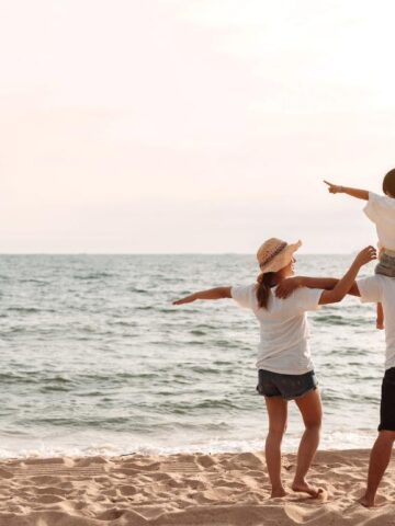 family of 3 walking along the beach, child on dad's shoulders