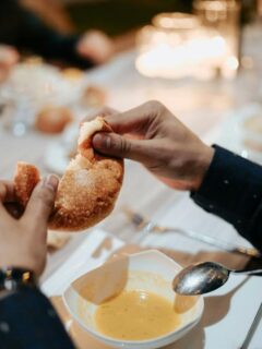 Family breaking bread over bowls of warm homemade soup during a candlelit dinner gathering.