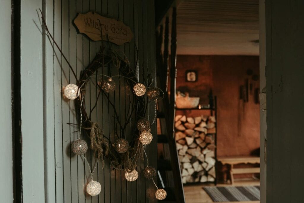 Open cabin doorway with warm string lights and a neatly stacked pile of firewood in the background.