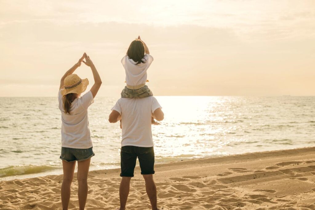 mom, dad, and child standing on beach looking at the sunlight reflecting on the water