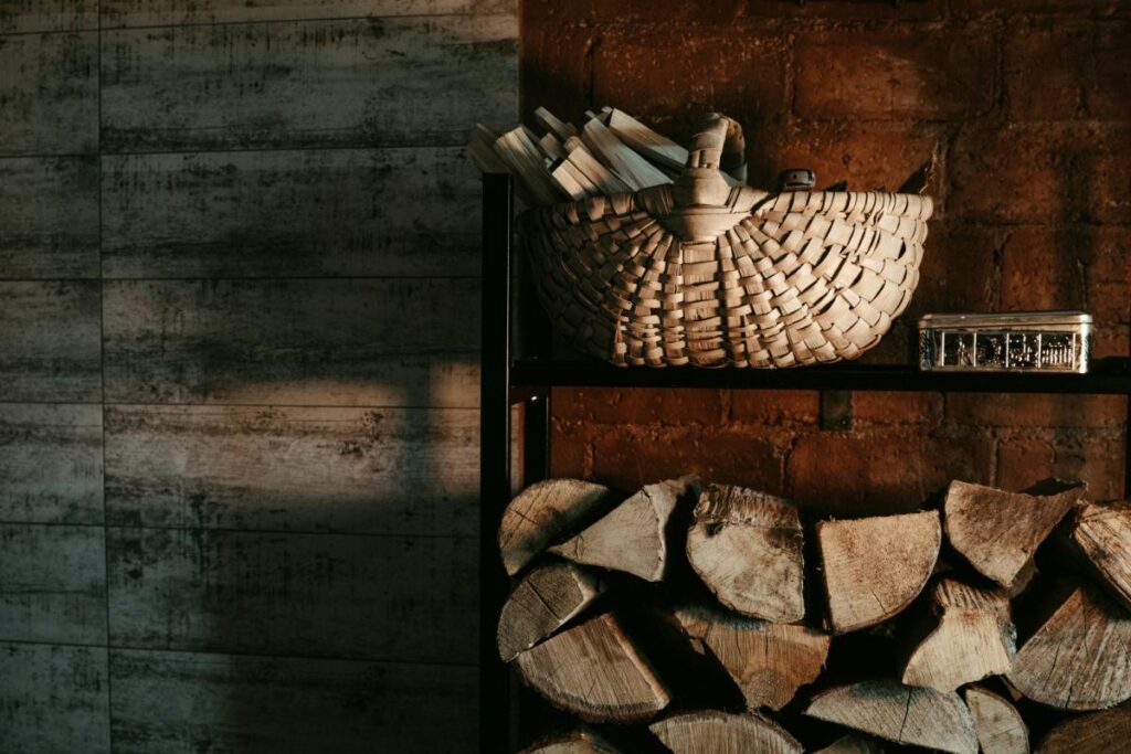 Basket of seasoned firewood stacked indoors against a brick wall near a fireplace.