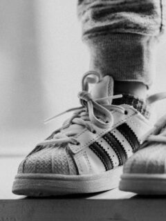 Close-up of classic low-profile Adidas-style sneakers on child’s feet, showing iconic stripes and timeless design