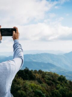 Woman taking a photo of the Smoky Mountains from a scenic overlook on a clear day, capturing layered blue mountain views.