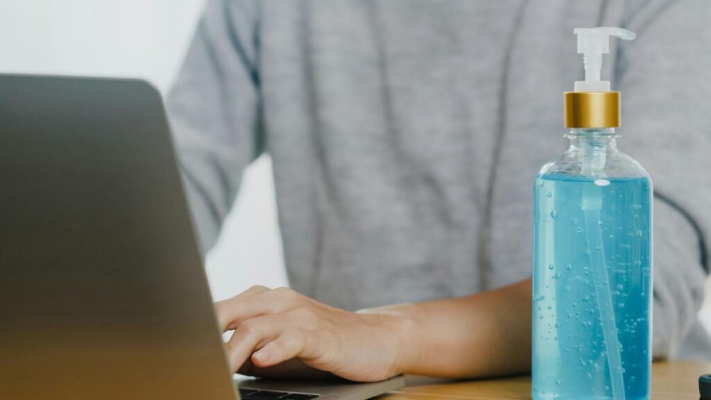 bottle of hand sanitizer in front of person using laptop