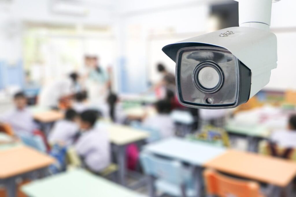 Security camera monitoring a classroom with students and a teacher in the background, representing modern school surveillance and campus safety technology.