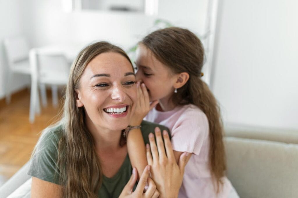 Mother smiling while daughter whispers in her ear, showing warm and positive family communication at home
