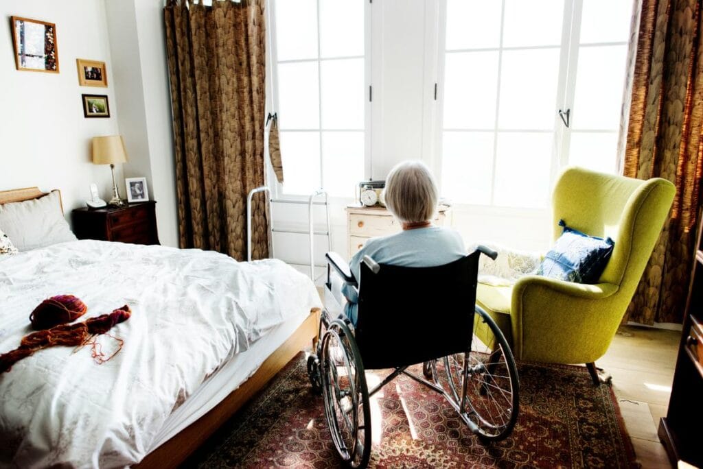elderly woman in wheelchair looking out bedroom window