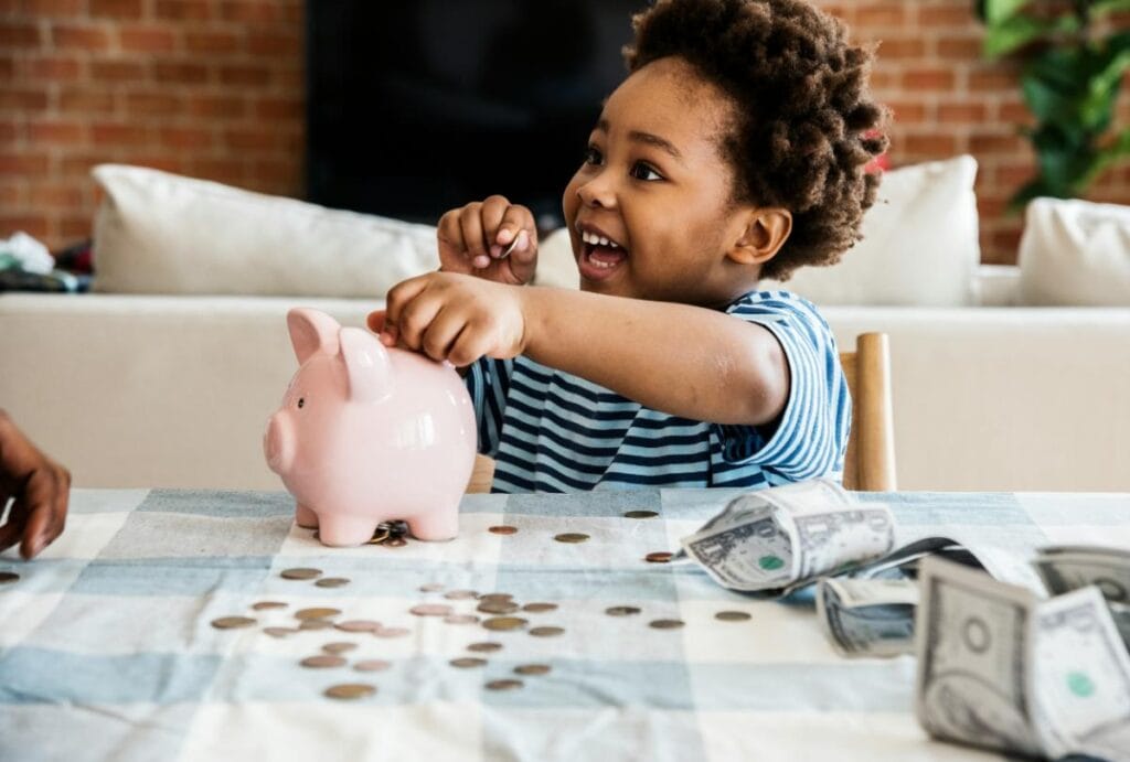 Child putting coins into a pink piggy bank while learning about saving money at home