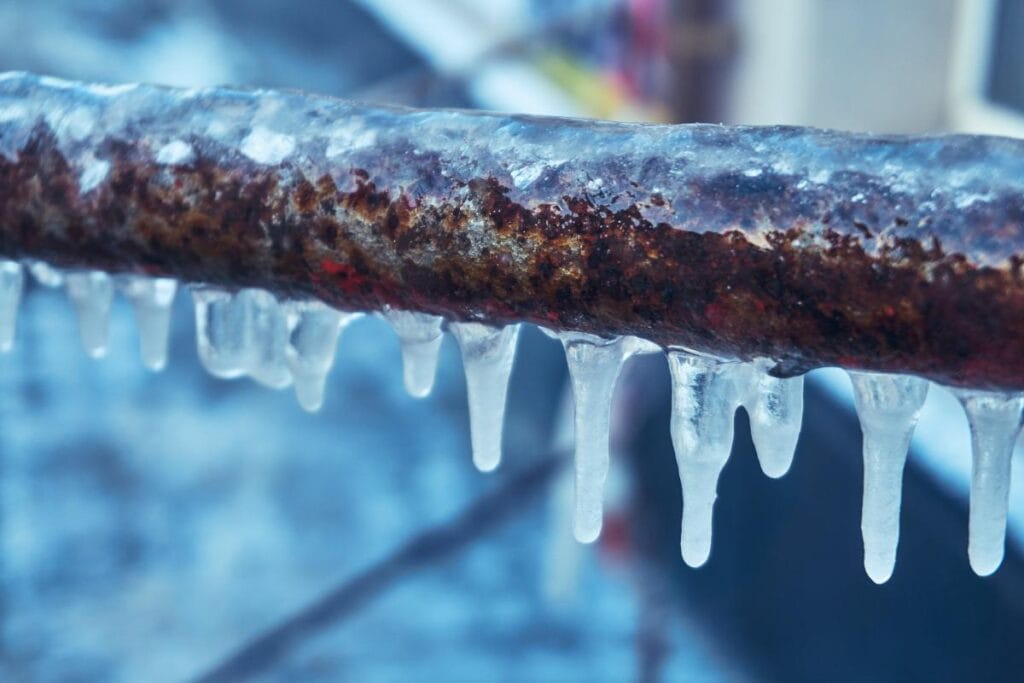 Rusty metal pipe covered in icicles showing signs of freezing winter temperatures.