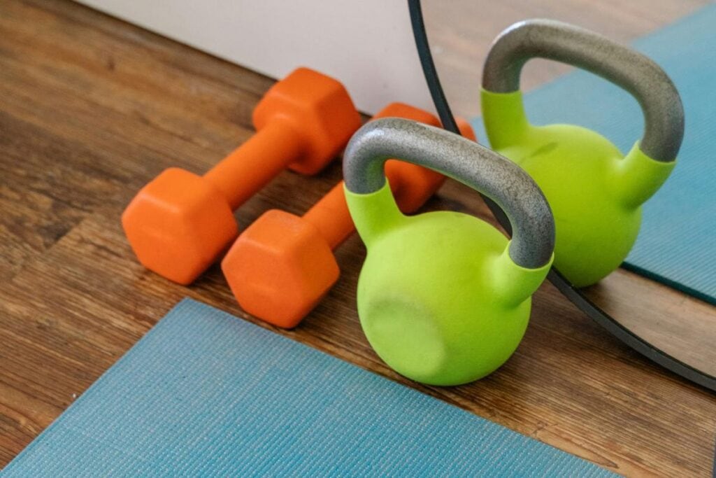 Kettlebells and dumbbells on a yoga mat in a home workout space with mirror reflection