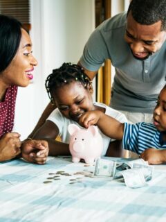 Parents helping children add coins to a piggy bank while teaching kids about saving and managing money