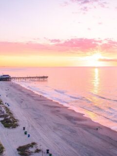 Sunrise over Myrtle Beach with the SkyWheel, sandy shoreline, and pier stretching into the Atlantic Ocean.