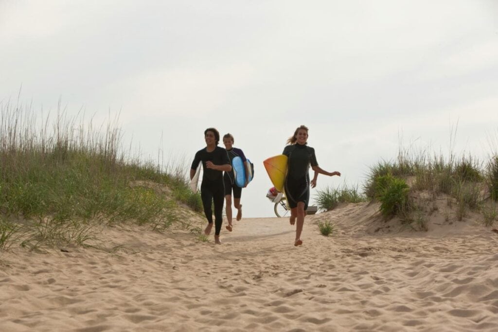 three people running on beach carrying surfboards