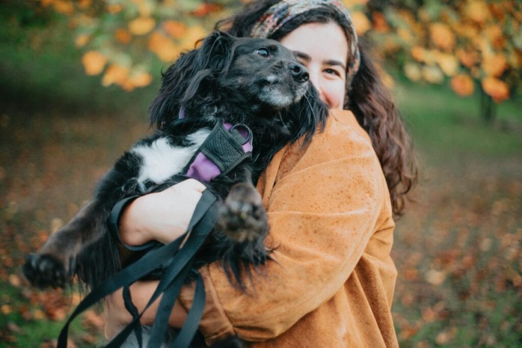 Woman holding a black dog outdoors in a park during autumn, showing the close bond between pet owners and their dogs.