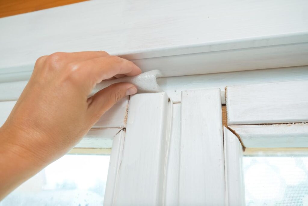 woman placing foam insulation above windows to block out air