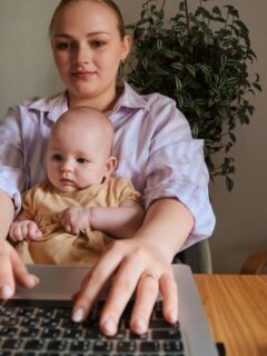 woman holding baby in lap while typing on laptop