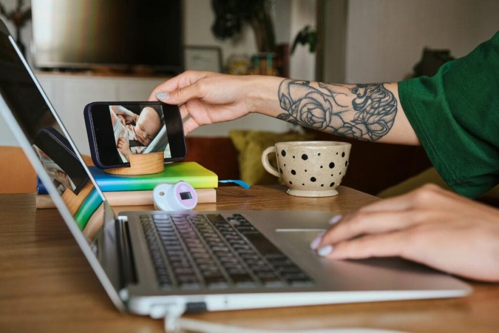 woman watching baby sleep on baby monitor while working from laptop