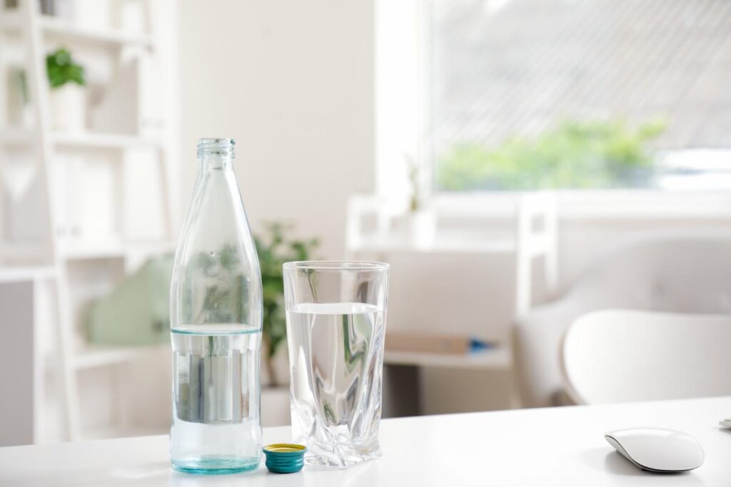 Hand pouring bottled water into a clear glass outdoors with a soft green background, highlighting freshness and everyday hydration.