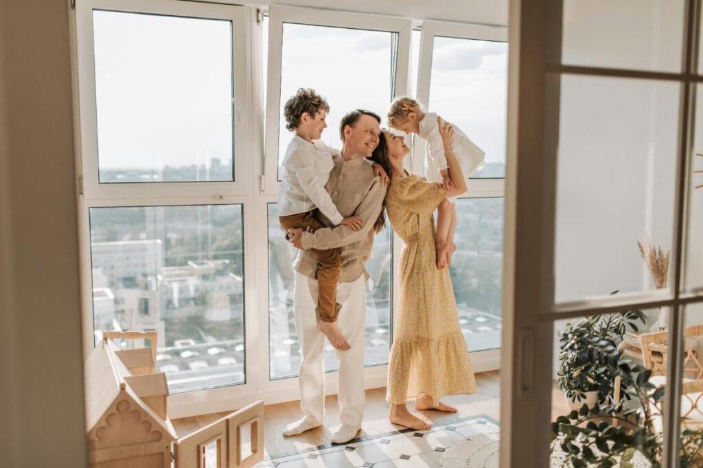 family of four embracing in front of windows in new apartment