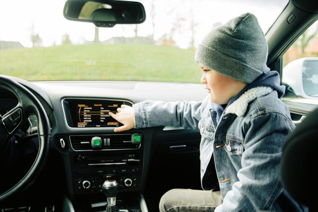 boy sitting in front seat pointing at screen in car