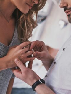 man placing engagement ring on woman's finger
