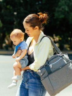 Mother carrying her baby and a spacious diaper bag outdoors, highlighting practical everyday organization for moms on the go.